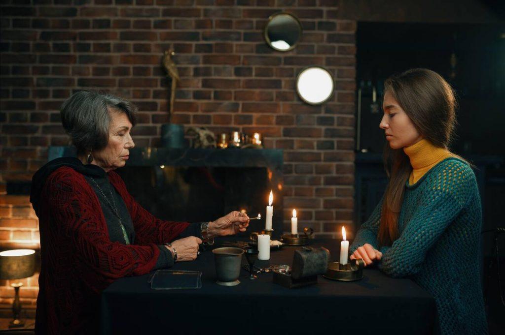 Una medium accende una candela seduta di fronte ad una donna che funge da sitter.